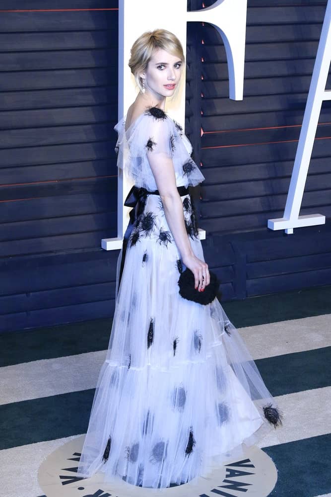 Emma Roberts attended the 2016 Vanity Fair Oscar Party on February 28, 2016 in Beverly Hills, California. She was seen wearing an elegant dress with her loose blonde bun hairstyle that has long side-swept bangs.