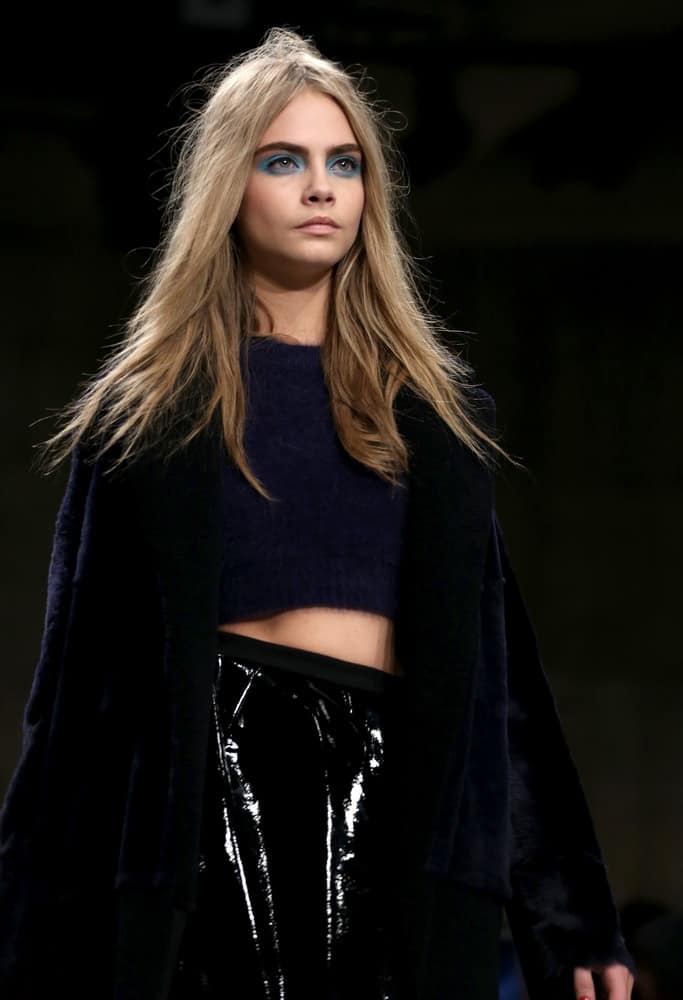 Cara Delevingne's center-parted loose and tousled sandy blond hairstyle was complemented by bold blue eye make-up at the Unique show as part of London Fashion Week AW13 in Tate Modern, London on February 17, 2013.