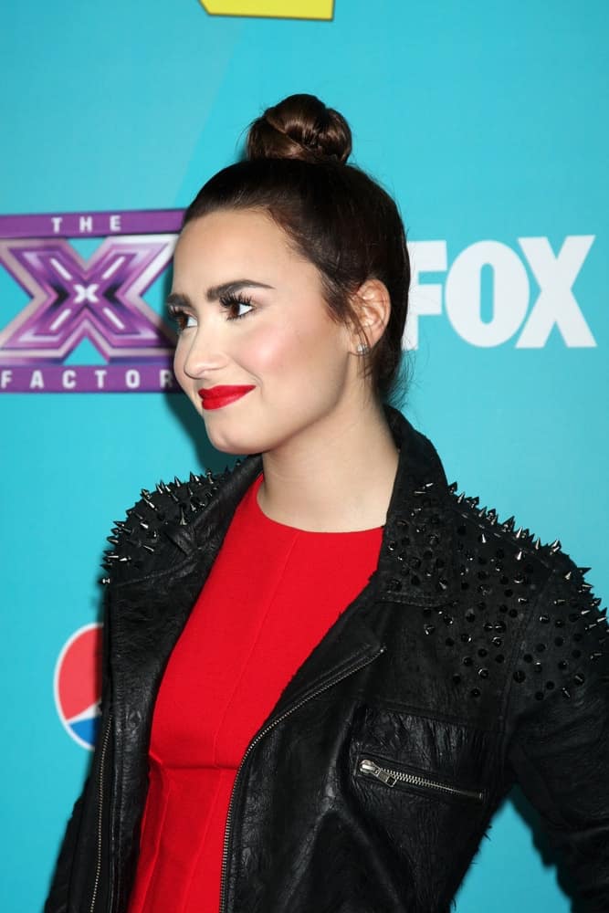 Demi Lovato wore a cool black leather jacket over her red dress to pair with her neat top knot bun hairstyle with some loose tendrils at the X-Factor Season Two Finalist Party at the SLS Hotel at Beverly Hills on November 5, 2012 in Los Angeles, CA.
