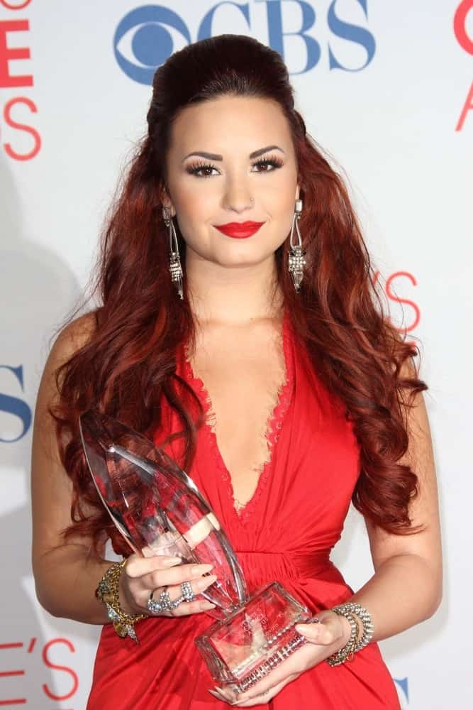 Demi Lovato was quite stunning with her red dress, red lips and red-dyed hairstyle in a half-up tousled hairstyle with waves and curls at the 2012 People's Choice Awards Press Room, Nokia Theatre in Los Angeles, CA on January 11, 2012.