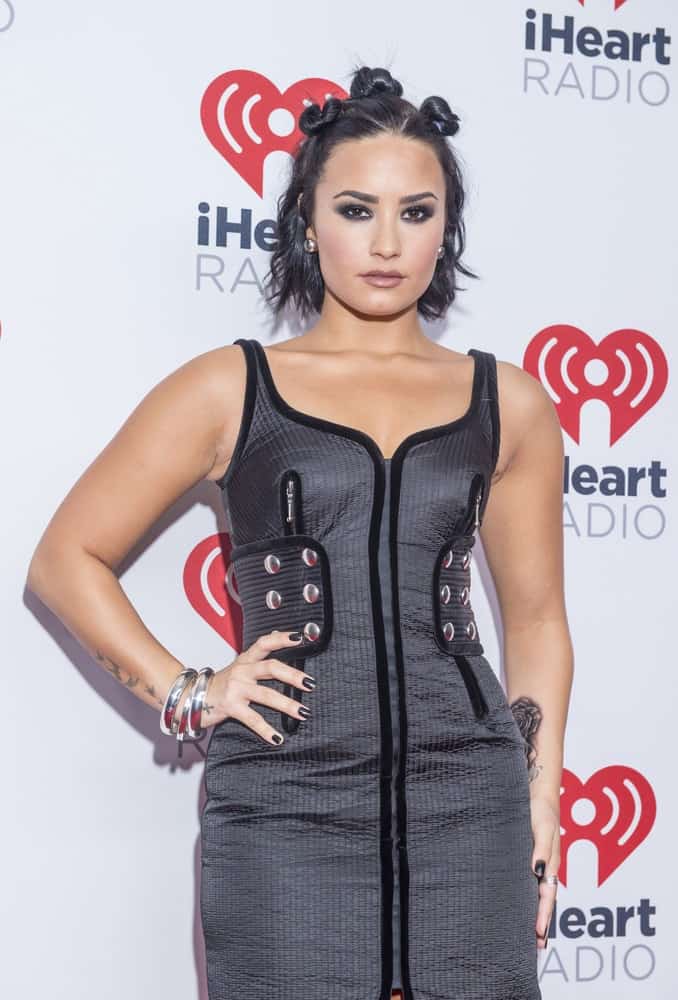 Singer and songwriter Demi Lovato attended the 2015 iHeartRadio Music Festival at the MGM Grand Garden Arena on September 18, 2015 in Las Vegas. She wore a lovely dark gray dress that she matched with her half-up short chin-length raven hairstyle with buns and waves.