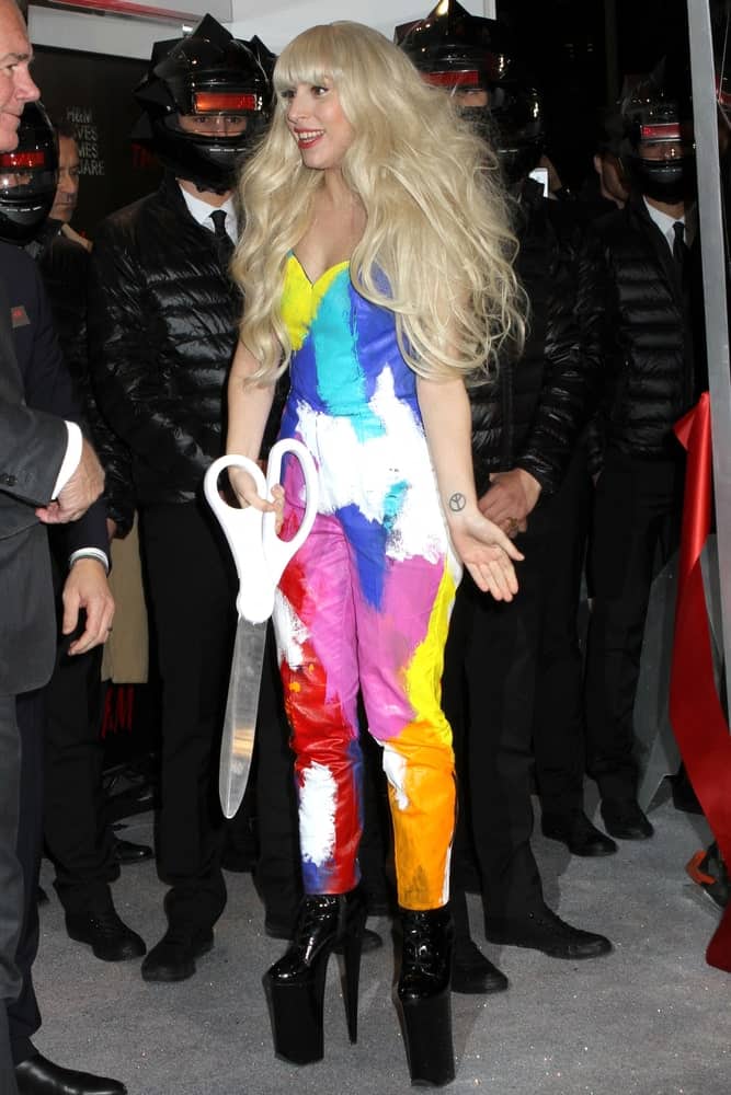 Lady Gaga looked quite lovely in her colorful body outfit, tall black heels and a thick, wavy and tousled blond hair with blunt bangs at the H&M Times Square store opening on November 14, 2013 in New York City.
