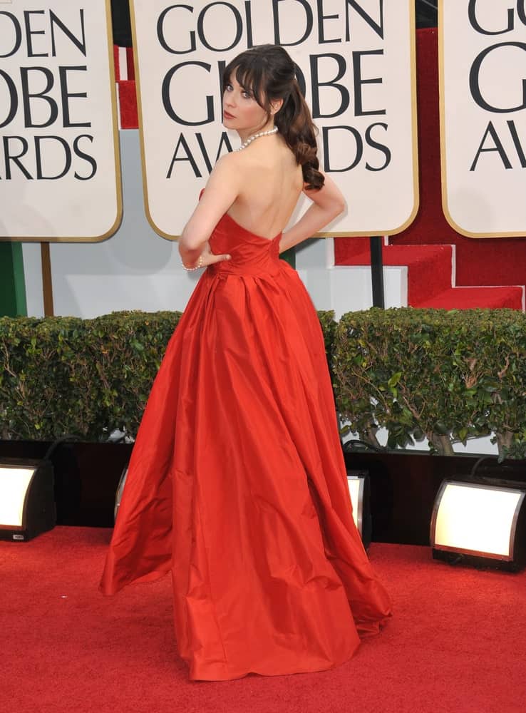 On January 13, 2013, Zooey Deschanel attended the 70th Golden Globe Awards at the Beverly Hilton Hotel. She was elegant in a red dress with her long clipped dark brunette wavy hairstyle with bangs.