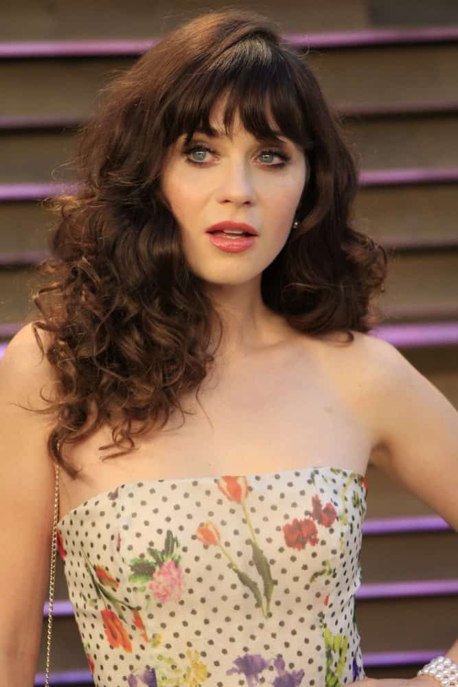 Zooey Deschanel was at the 2014 Vanity Fair Oscar Party on March 2, 2014 in West Hollywood, California. She paired her stunning floral strapless dress with a tousled curly brunette hairstyle with blunt bangs.