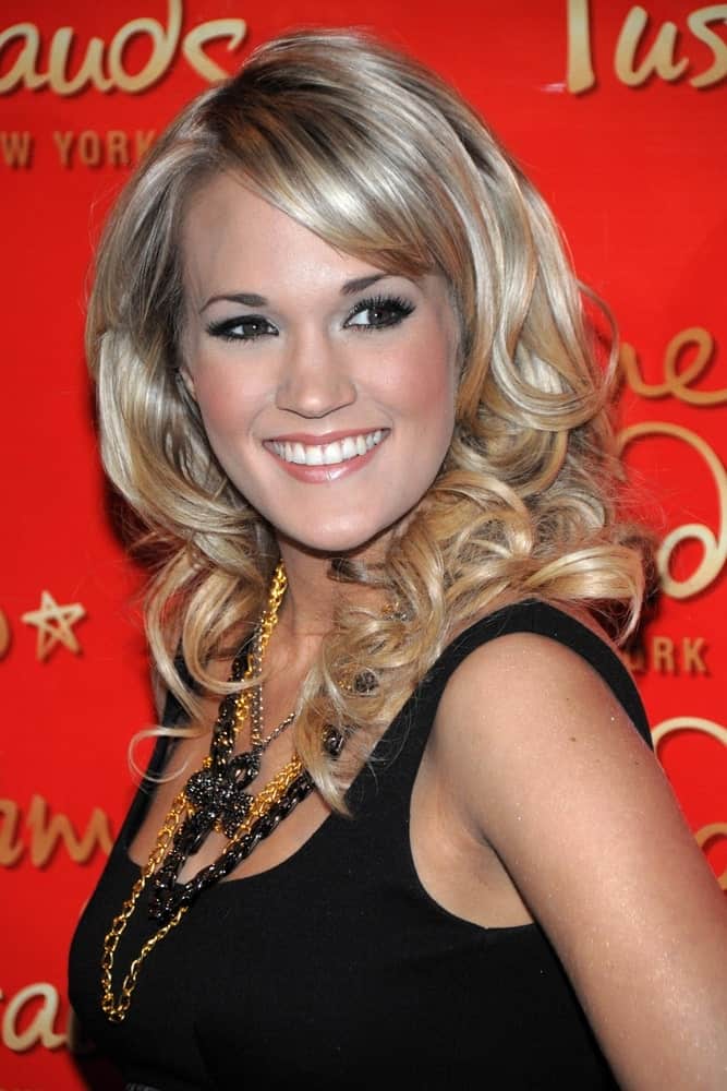Carrie Underwood arrived at an in-store appearance for the Unveiling of Carrie Underwood Wax Figure on October 22, 2018. She styled her highlighted blonde curls with a side part and bangs to pair with her black dress and layered necklaces.