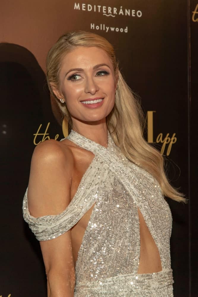 Paris Hilton flashed a sweet smile with her pinned side-parted hairstyle at The Glam App and Paris Hilton Launch Party on June 19, 2019. A sequined halter dress completed the gorgeous look.