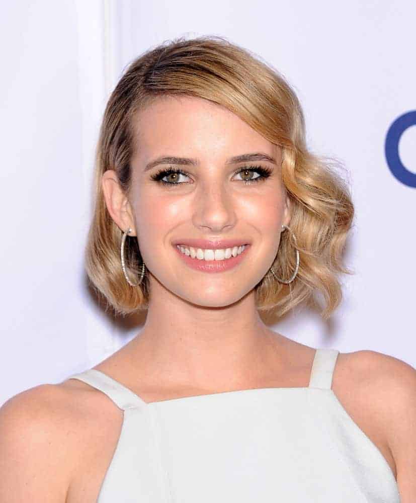 Emma Roberts was at the Paleyfest 2014: American Horror Story COVEN on March 28, 2014 in Hollywood, CA. She wore a white dress that she topped with a chin-length tousled blonde hairstyle with vintage curls and side-swept bangs.