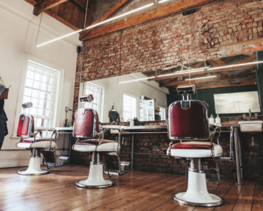 Stunning barber shop interior with tall ceiling, brick wall, old school chairs and wood floor.