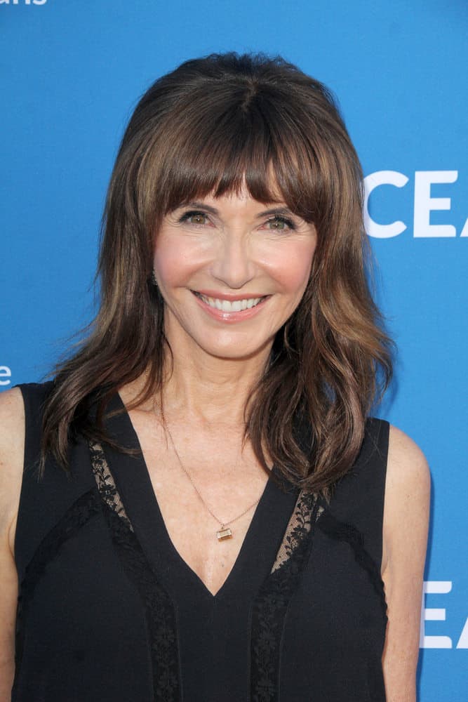 The seventh hairstyle is worn by Mary Steenburgen. The hairstyle features bangs, giving the wearer a more youthful look. Along with the bangs, the long, deep auburn-colored layers of hair are tousled waves going in different directions, adding more volume to the hair. 