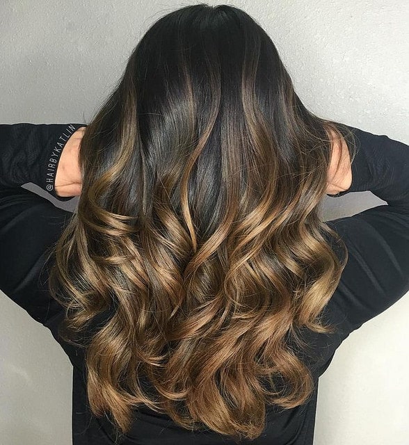 This young woman has created a dark blonde and caramel effect on her black hair. The stunning glossy gold and brown shades on her dark hair look like melted bronze has been poured over her tresses