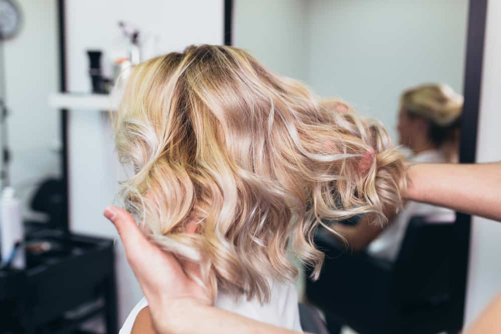 A stylist fluffing out the short curly blond hair of a client