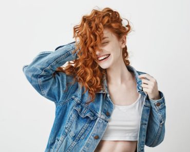 A red-haired girl smiles and touches her curls on a white background