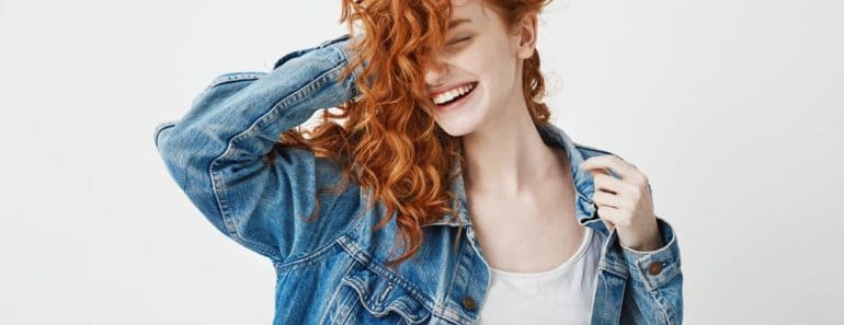 A red-haired girl smiles and touches her curls on a white background