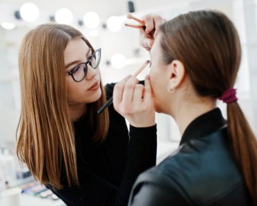A makeup artist applies eyeshadow on a woman.
