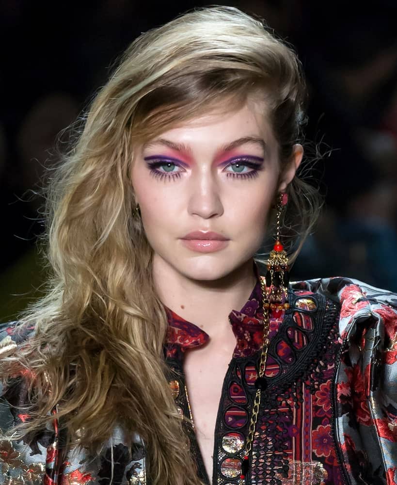 On February 12, 2018, Gigi Hadid walked the runway at the Anna Sui Fall Winter 2018 fashion show during New York Fashion Week. Her beautiful hair was styled into a tousled wavy side-swept hairstyle with highlights.