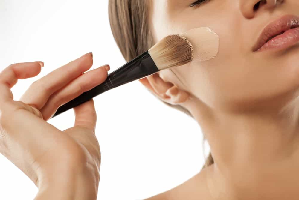 A woman applying brush makeup on her face.