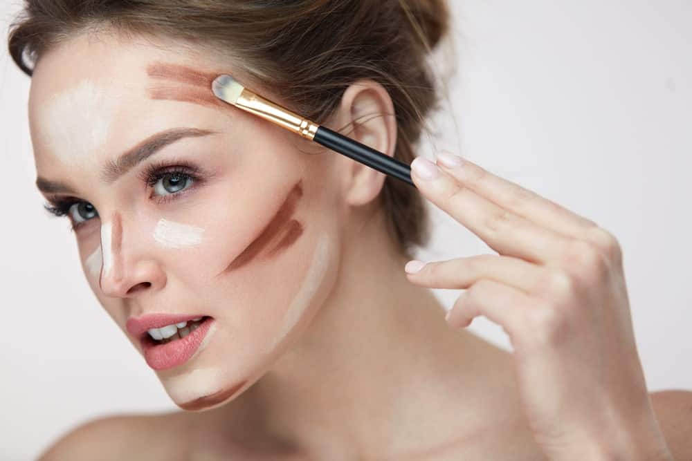 A woman applying blush and bronzer to her face with a brush.