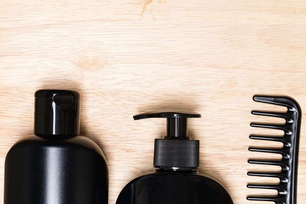 Hair care products along with a wide tooth comb against the wooden surface.